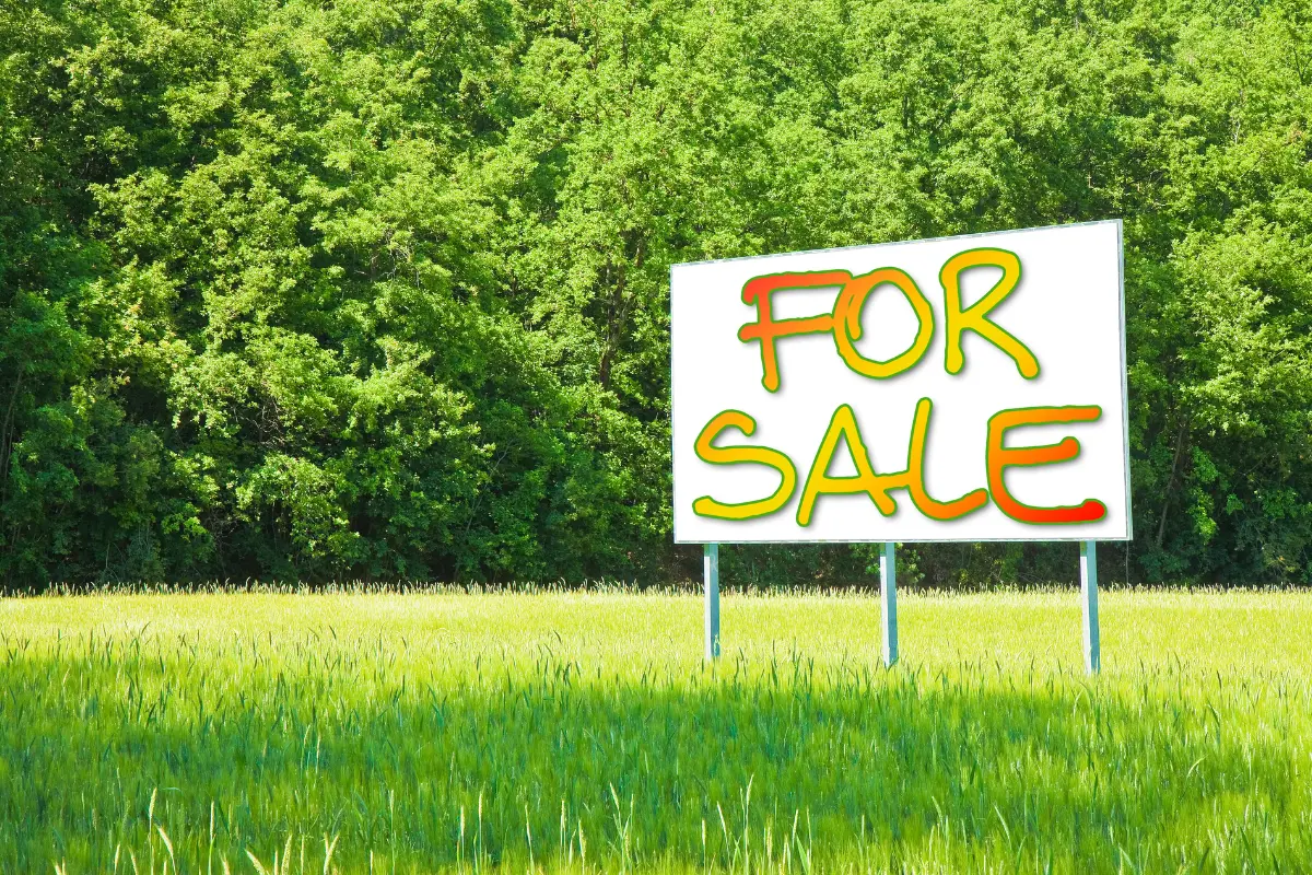 Descubra como vender terreno comercial de forma rápida. Placa de “Vende-se” em destaque com fundo urbano desfocado. Foto: Reprodução / Canva Pro.